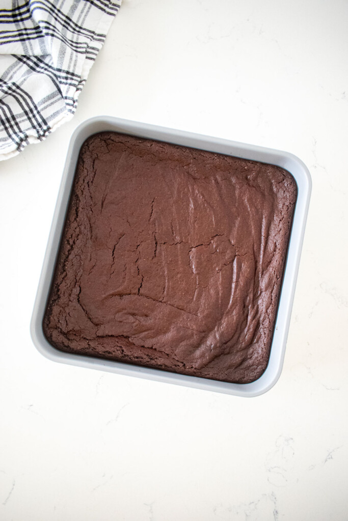 baked eggless brownies in a square pan on a marble counter.