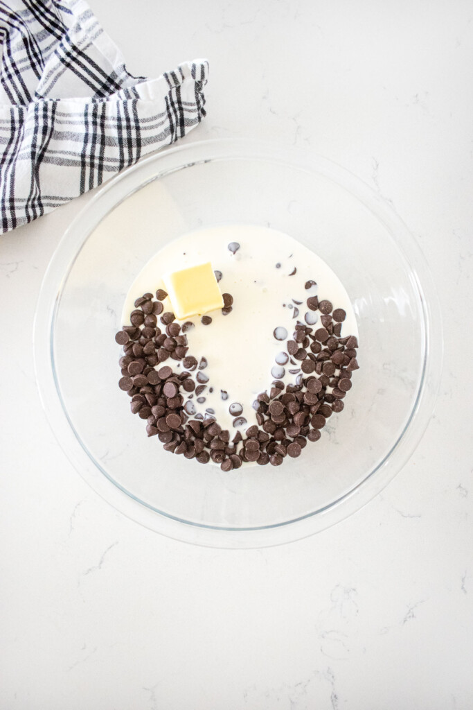 chocolate chips, cream and butter in a glass mixing bowl on a white marble counter.