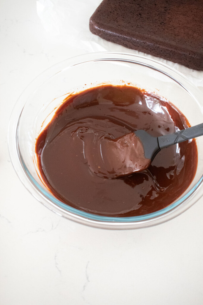 chocolate ganache in a glass mixing bowl with a spatula on a white marble counter.