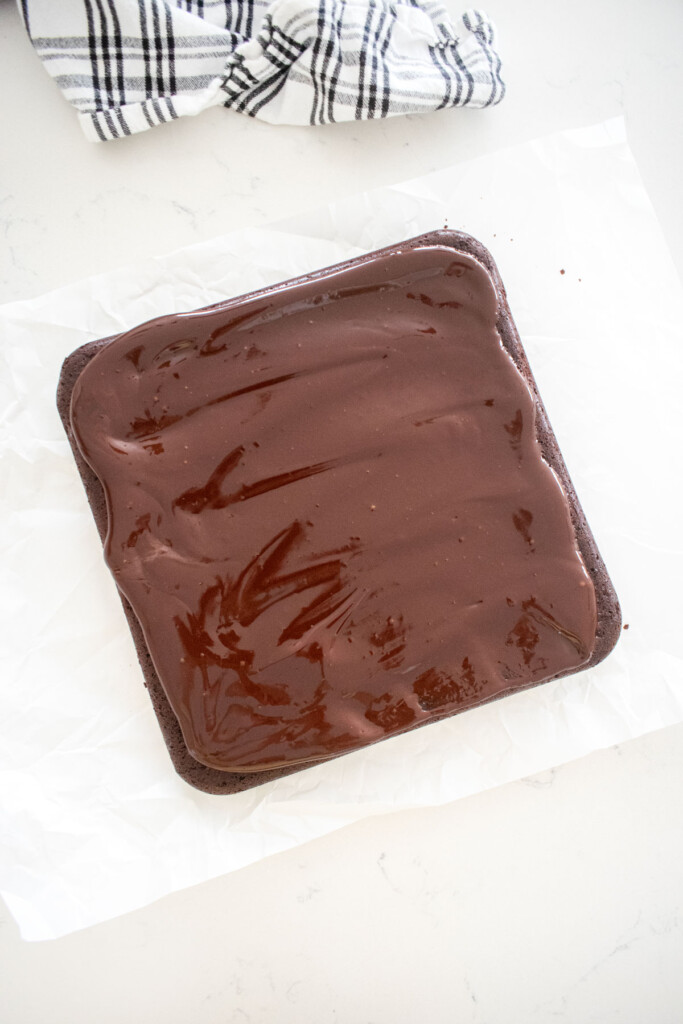 chocolate ganache spread onto brownies on a white marble counter.