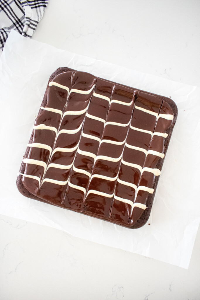 eggless chocolate ganache brownies with white chocolate chevron pattern on top on a white marble counter.