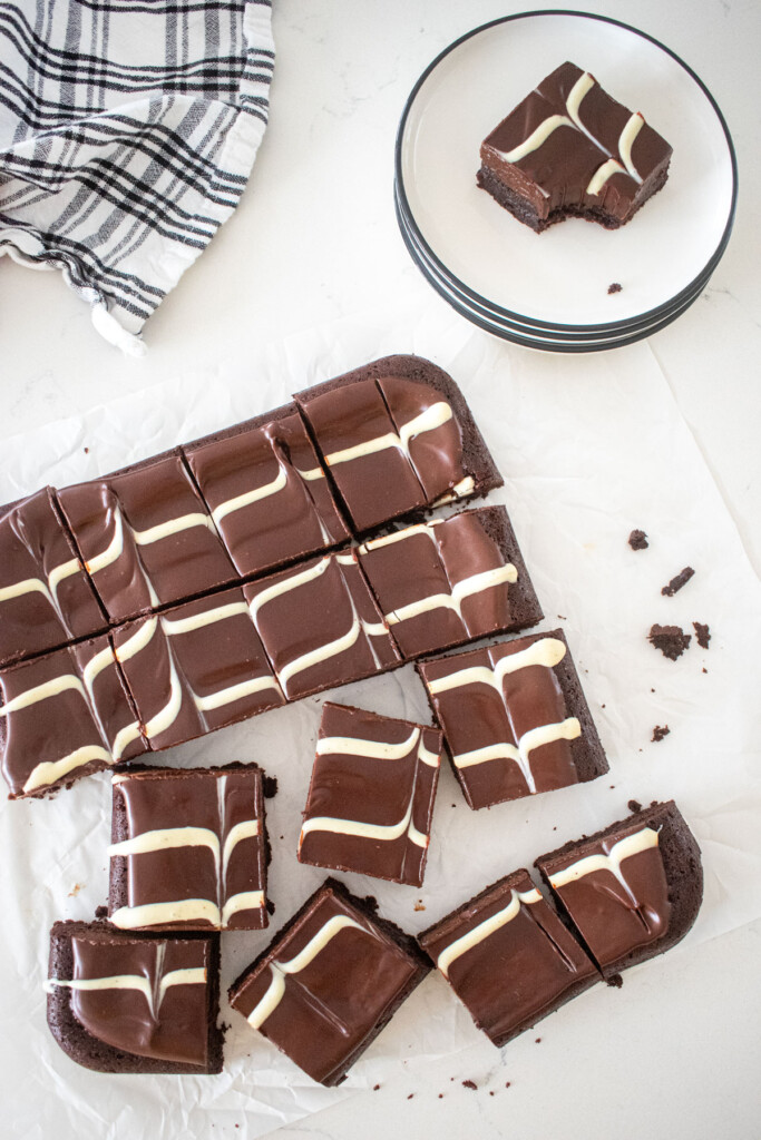 eggless chocolate ganache brownies with a white chocolate chevron design on top cut into small squares on a white marble counter.