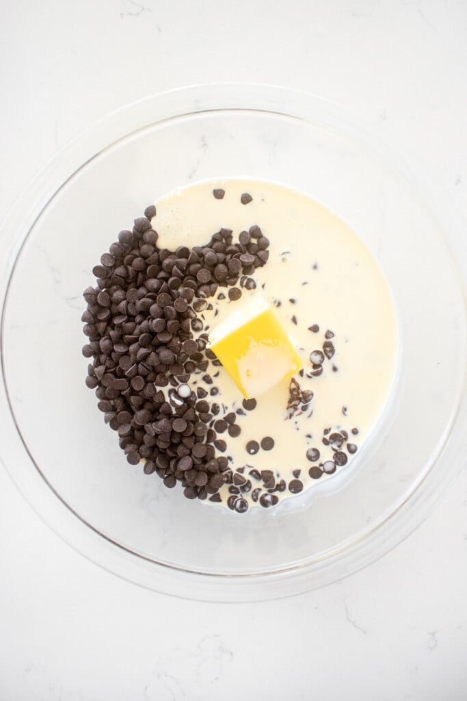 chocolate butter and cream in a glass mixing bowl on a white marble counter.