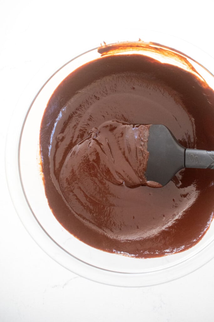 chocolate ganache in a glass mixing bowl on a white marble counter.