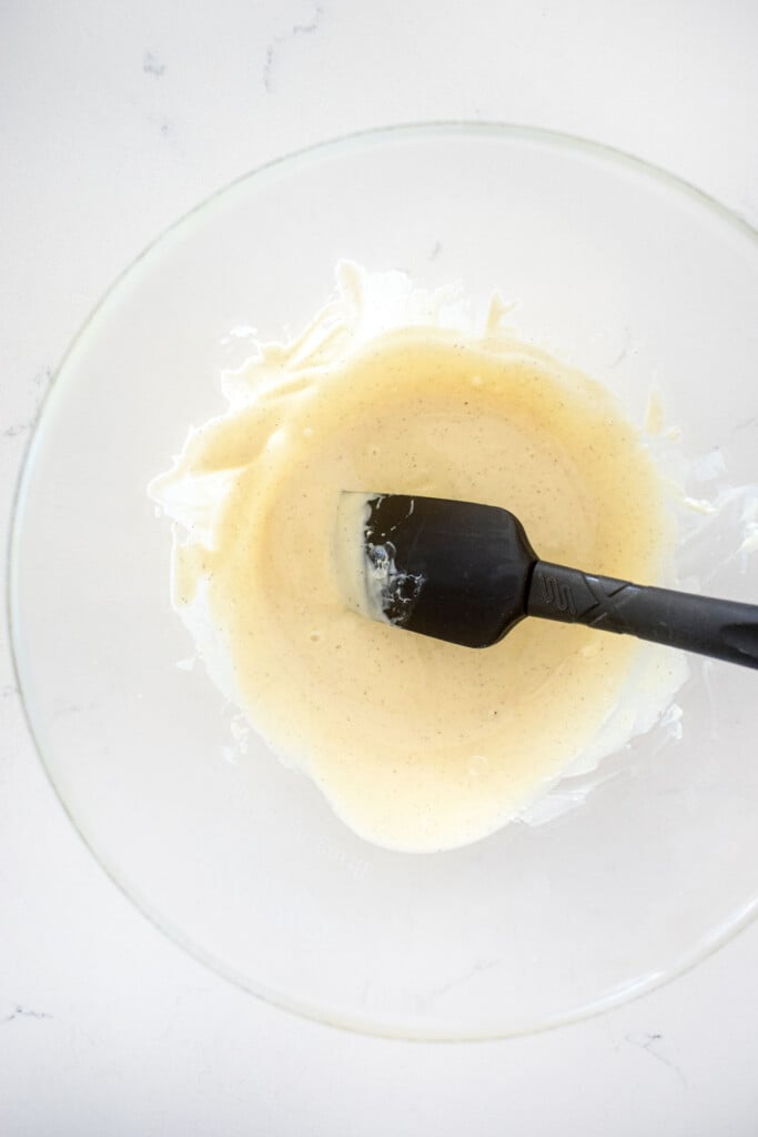 melted white chocolate chocolate in a glass mixing bowl on a white marble counter.
