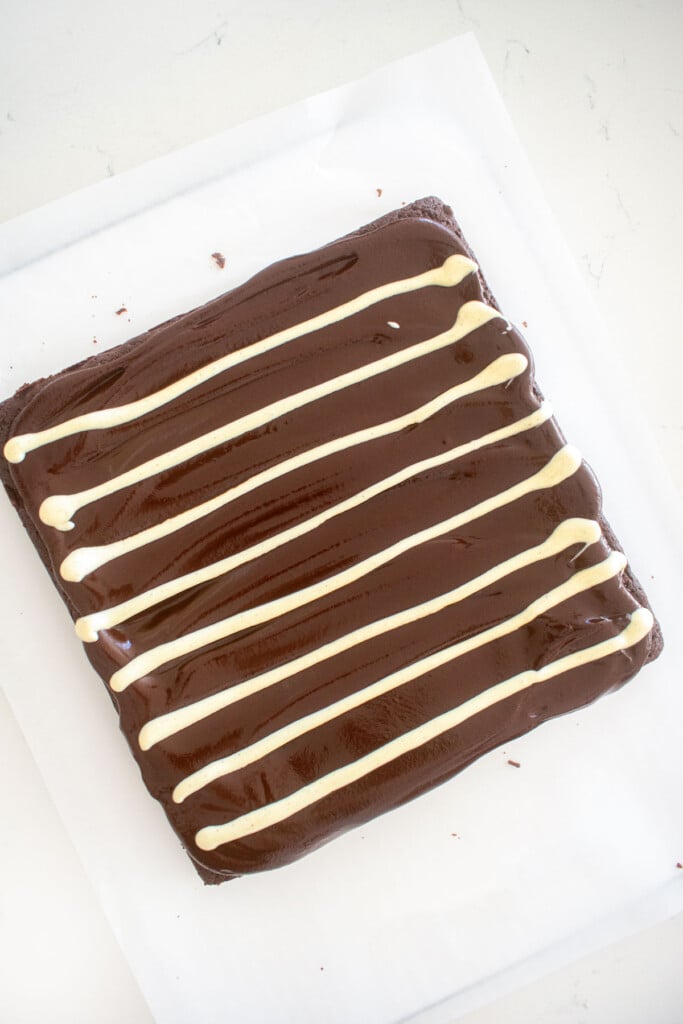eggless chocolate ganache brownies with white chocolate stripes on a white marble counter.