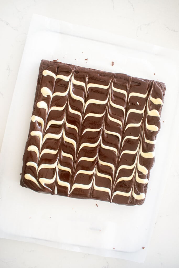 eggless chocolate ganache brownies with a white chocolate chevron design on a white marble counter.