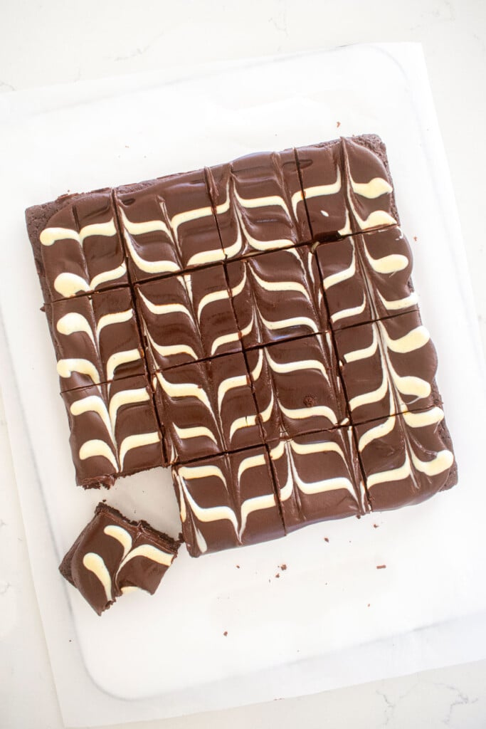 eggless chocolate ganache brownies cut into squares with a white chocolate chevron design on a white marble counter.