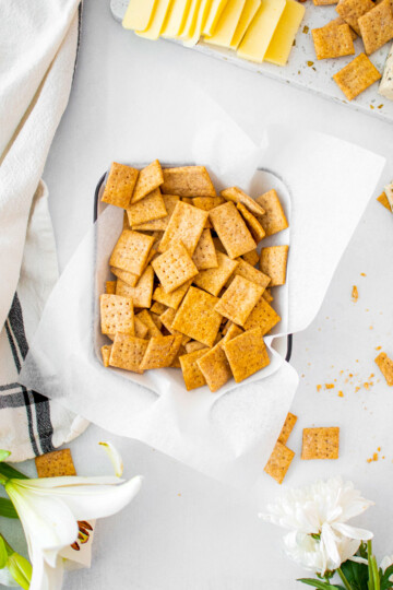 homemade sourdough whole wheat crackers in a serving dish on a table with flowers and cheese.