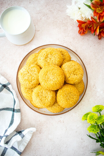 plate of olive oil shortbread cookies on a table with a mug of milk and fresh flowers.