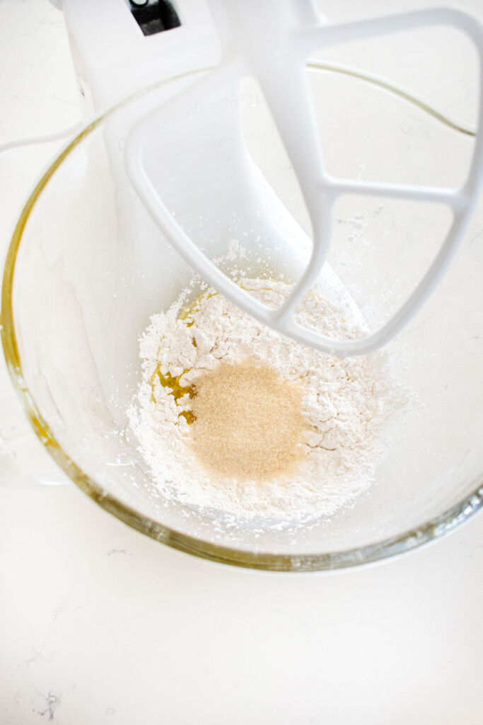 ingredients for olive oil shortbread cookies in a glass mixing bowl on a white marble counter.