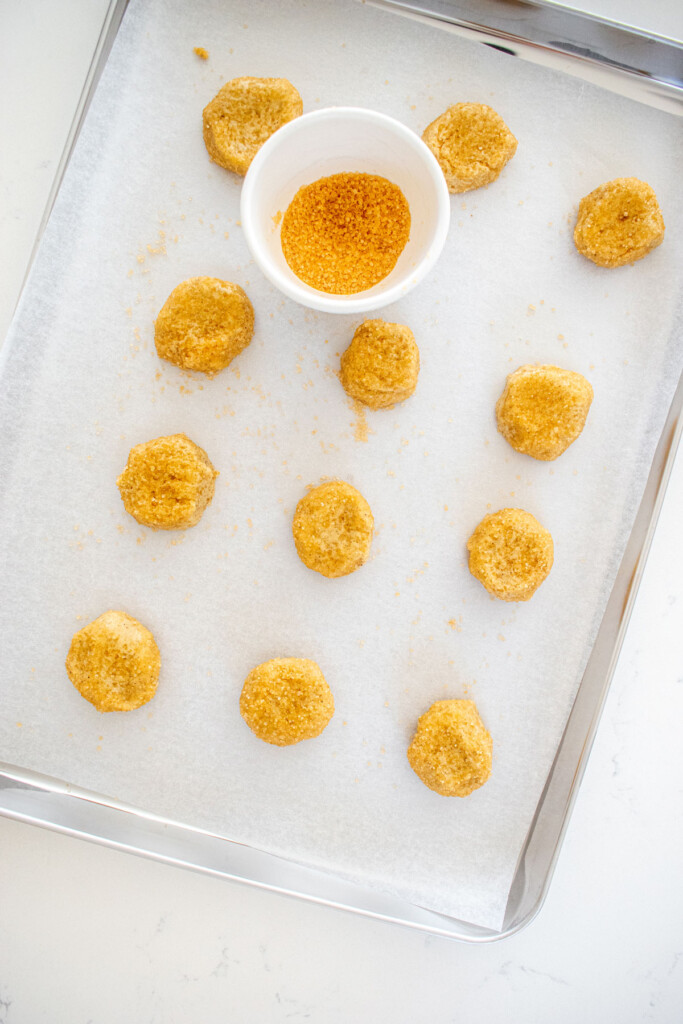olive oil shortbread cookie dough rolled in turbinado sugar spaced evenly apart on a baking sheet on a white marble counter.