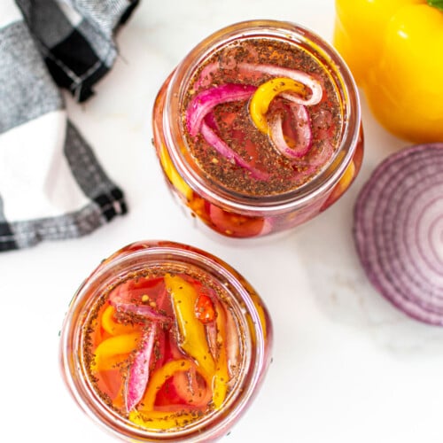 pickled onions and peppers in two mason jars on a white marble countertop.