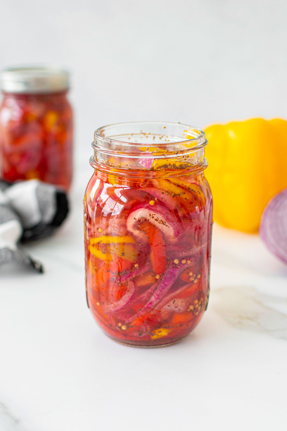 pickled onions and peppers in a mason jars on a white marble countertop.