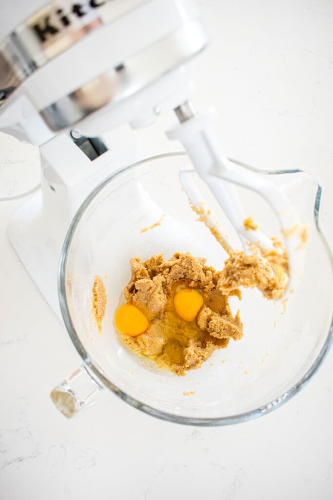creamed butter and sugar with eggs in a glass mixing bowl on a marble counter.
