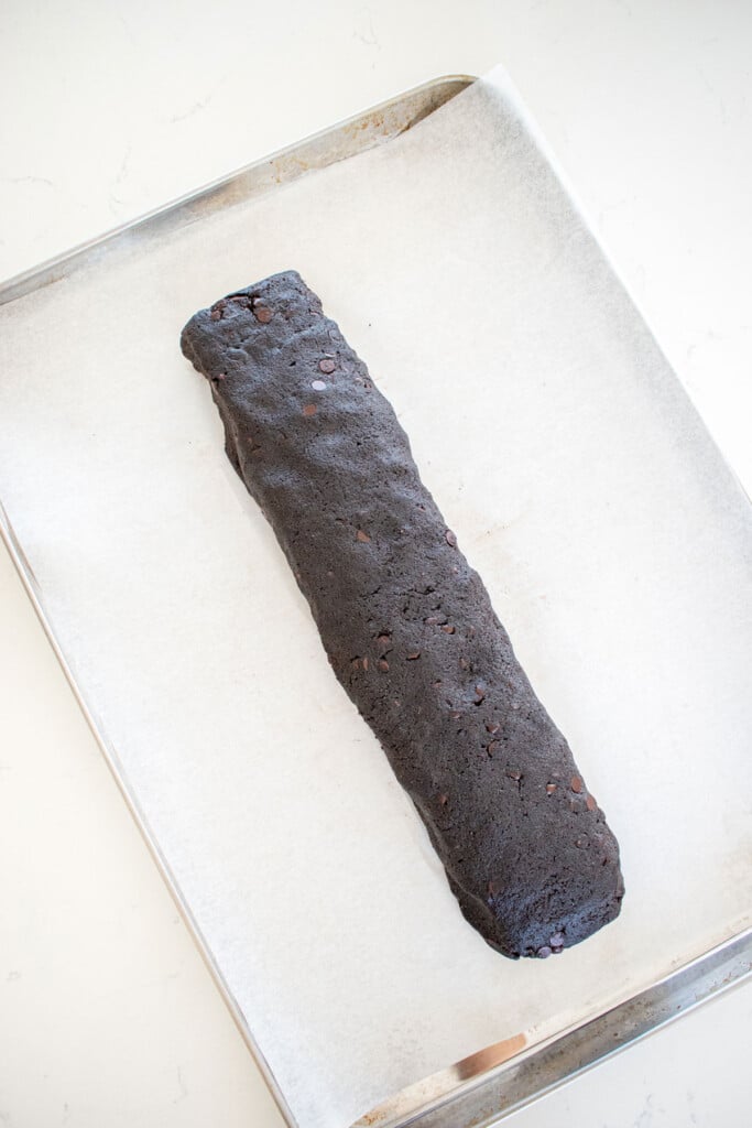 sea salt black cocoa biscotti cookie dough log on a baking sheet on a marble counter.