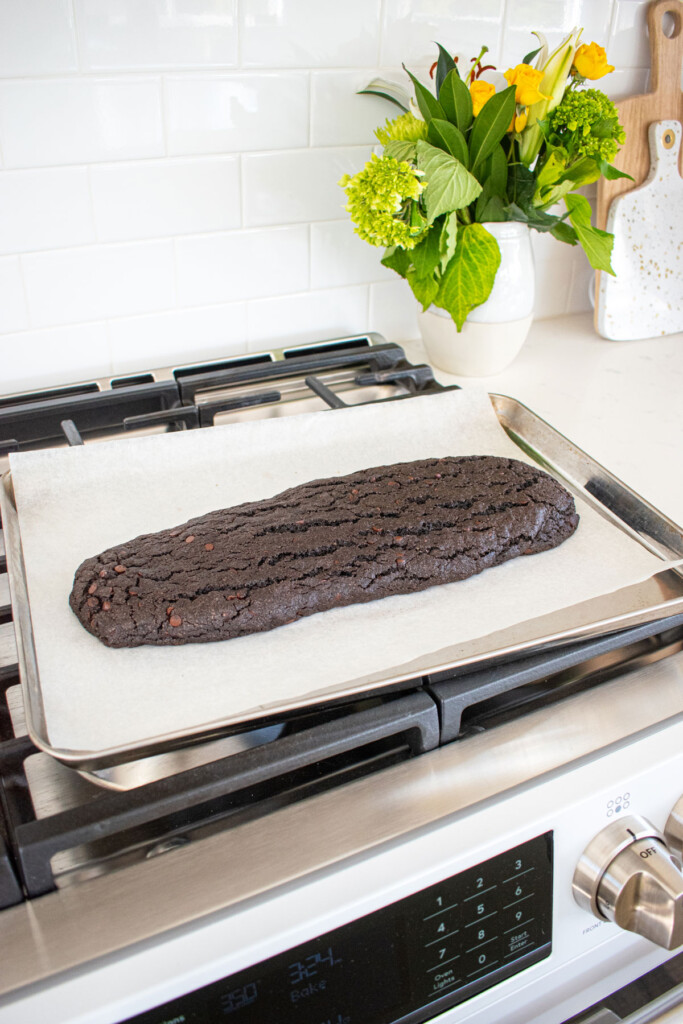 baked sea salt black cocoa biscotti log on a baking sheet cooling on top of an oven.
