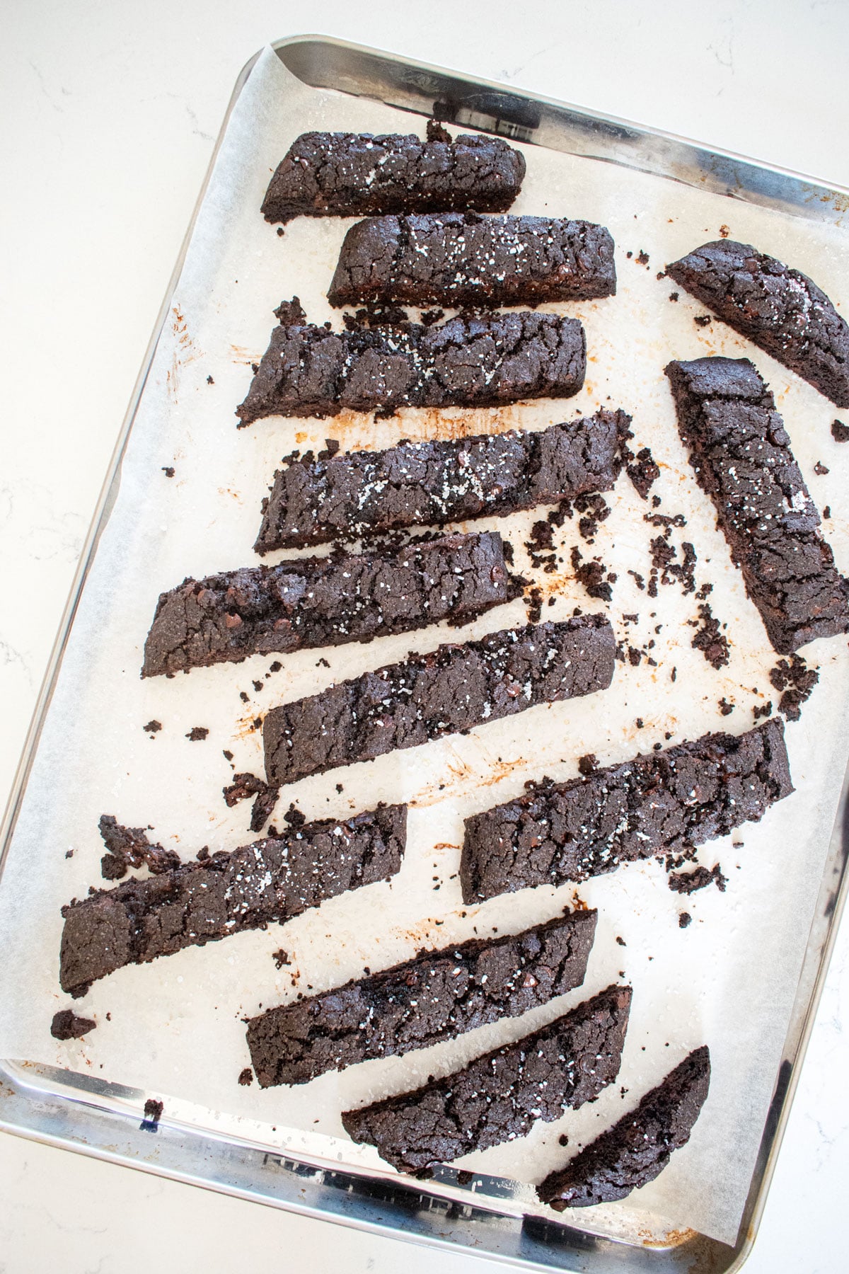 sea salt black cocoa biscotti pieces on a baking sheet on a marble counter.