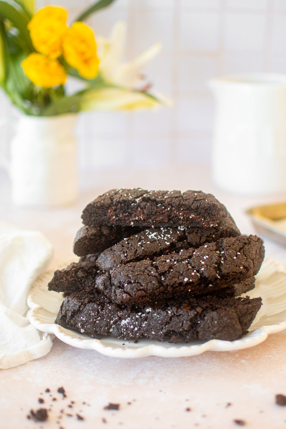 plate of sea salt black cocoa biscotti on a table with a vase of flowers.