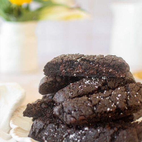 plate of sea salt black cocoa biscotti on a table with a vase of flowers.