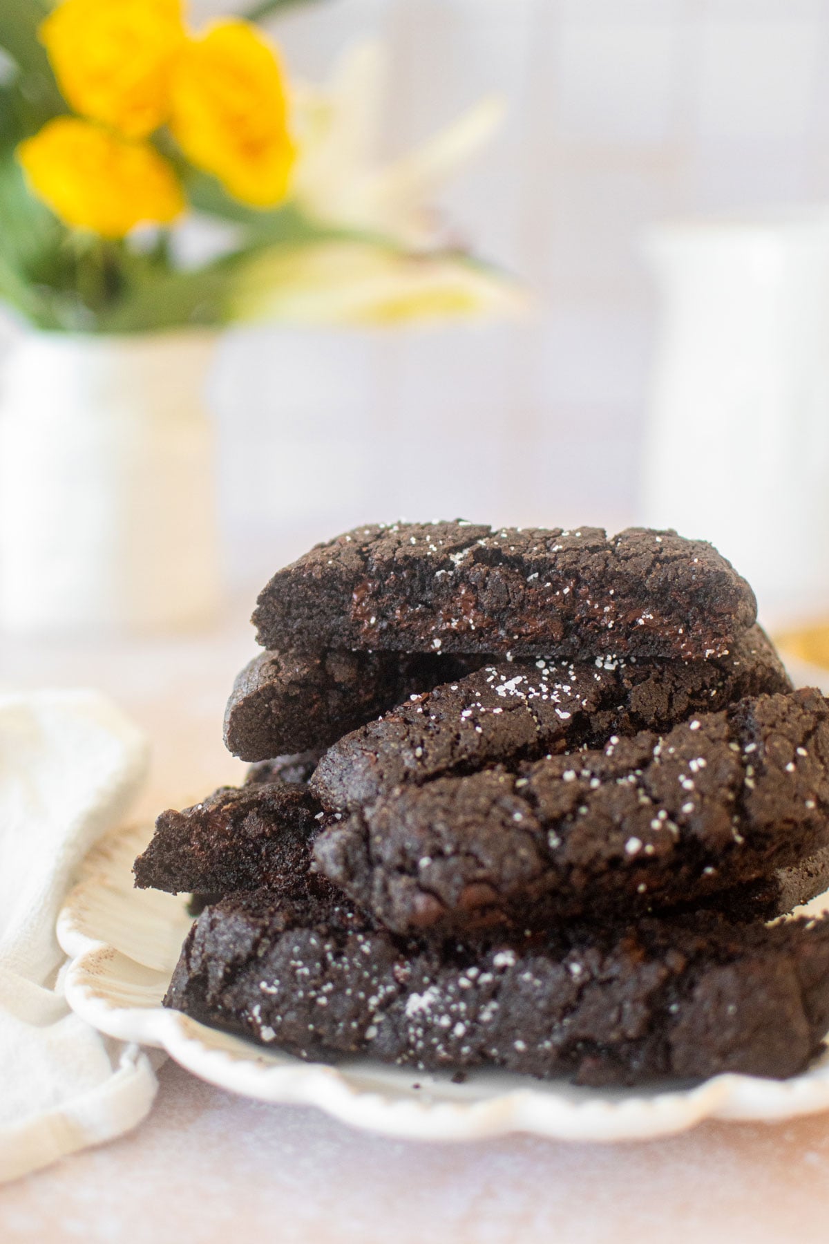 plate of sea salt black cocoa biscotti on a table with a vase of flowers.