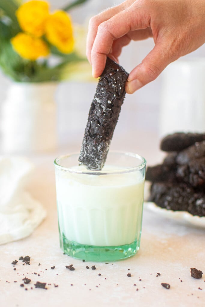glass of milk with a sea salt black cocoa biscotti being dipped into it.