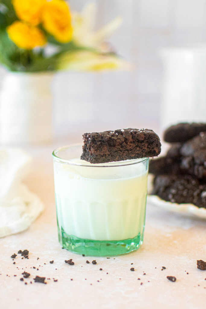 glass of milk with a sea salt black cocoa biscotti sitting on top on a table.
