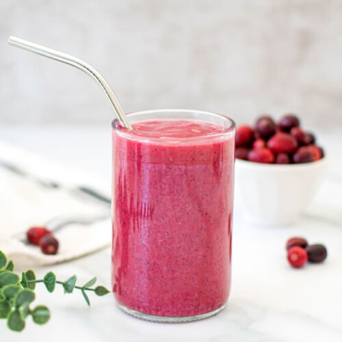 tropical cranberry smoothie in a glass with a metal straw on a marble countertop.