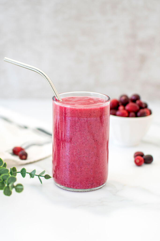 tropical cranberry smoothie in a glass with a metal straw on a marble countertop.