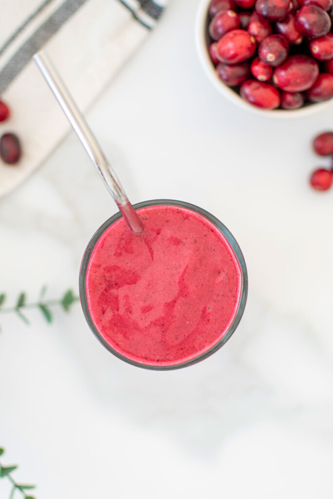 tropical cranberry smoothie in a glass with a metal straw on a marble countertop.