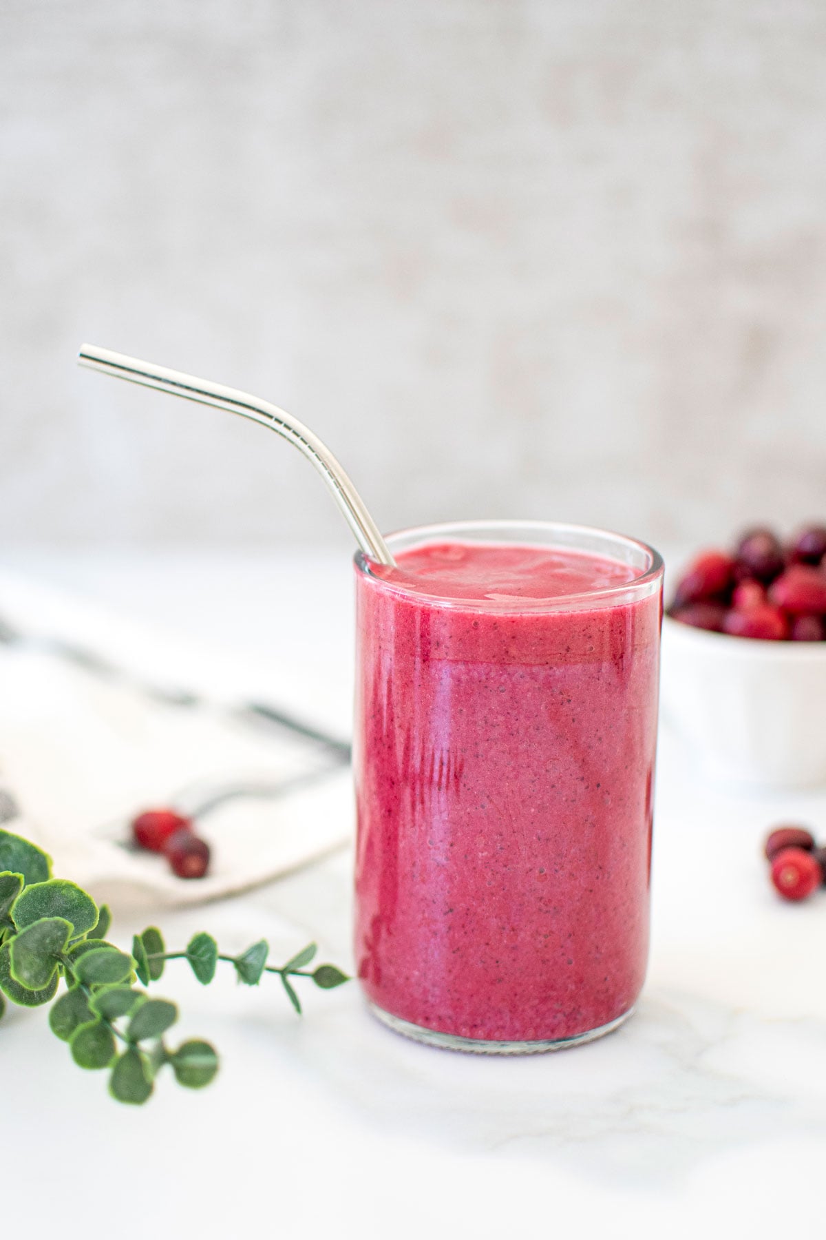 tropical cranberry smoothie in a glass with a metal straw on a marble countertop.