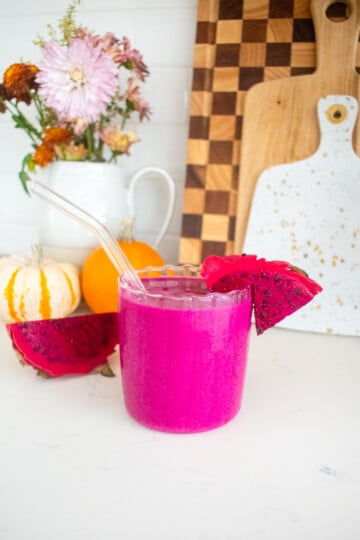 glass with tropical cranberry smoothie on a kitchen counter with a slice of dragon fruit in it.