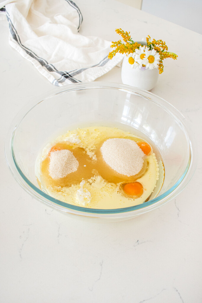 wet ingredients for vanilla buttermilk sheet cake in a glass mixing bowl on a marble counter with fresh flowers.