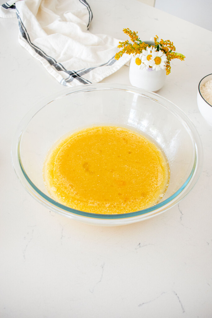 wet ingredient for vanilla buttermilk sheet cake mixed together in a glass mixing bowl on a marble counter with fresh flowers.