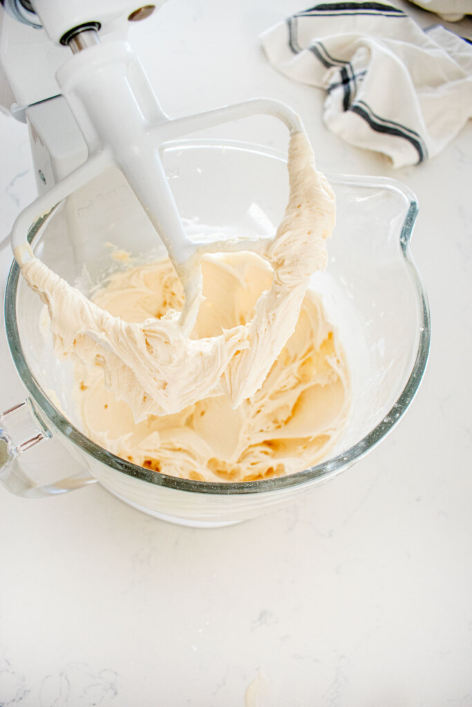 fluffy vanilla icing in a glass mixing bowl of a stand mixer on a marble counter.