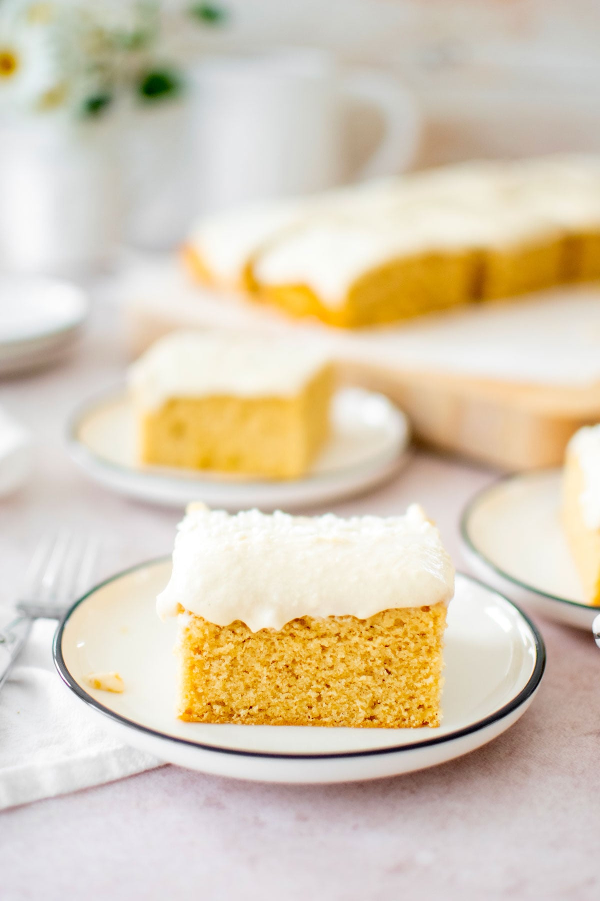 square slice of vanilla buttermilk sheet cake with vanilla frosting on a cake plate.