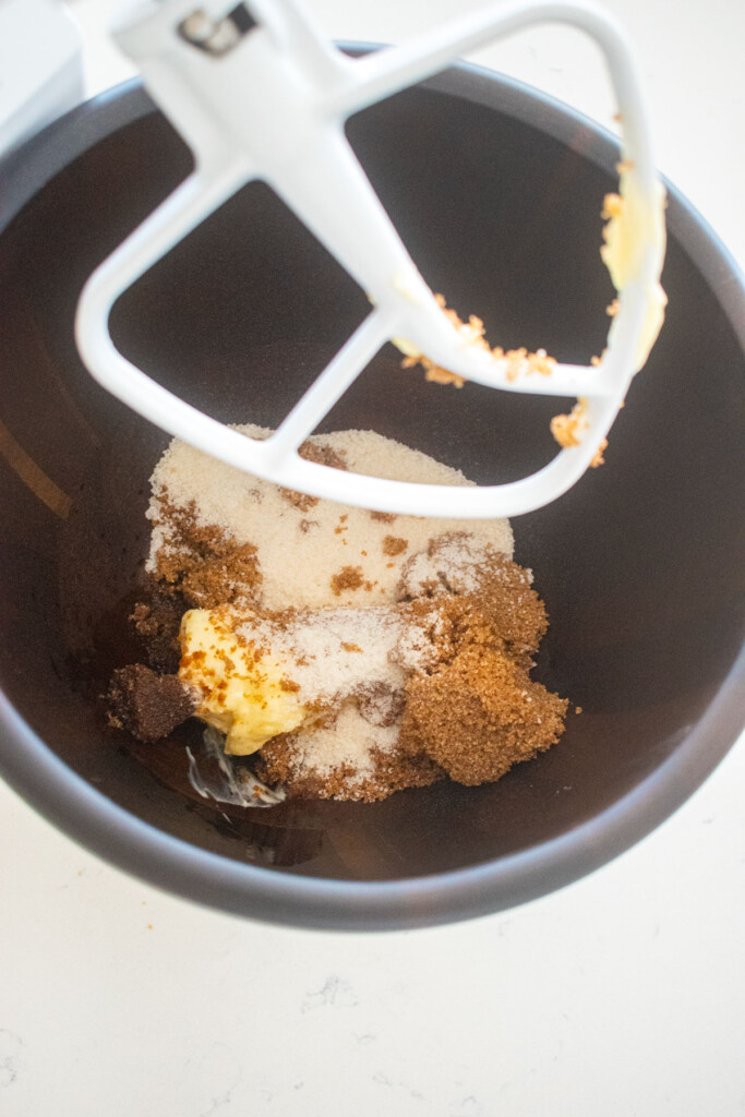 butter, brown sugar and cane sugar in a wood mixing bowl on a white marble counter.