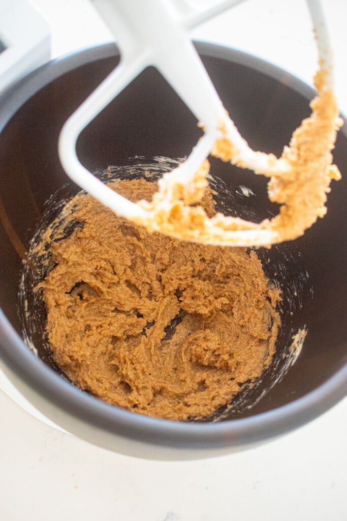 creamed butter, brown sugar and cane sugar in a wood mixing bowl on a white marble counter.
