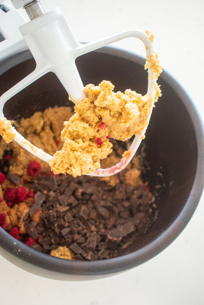 vegan raspberry chocolate chip cookie dough in a wood mixing bowl on a white marble counter.