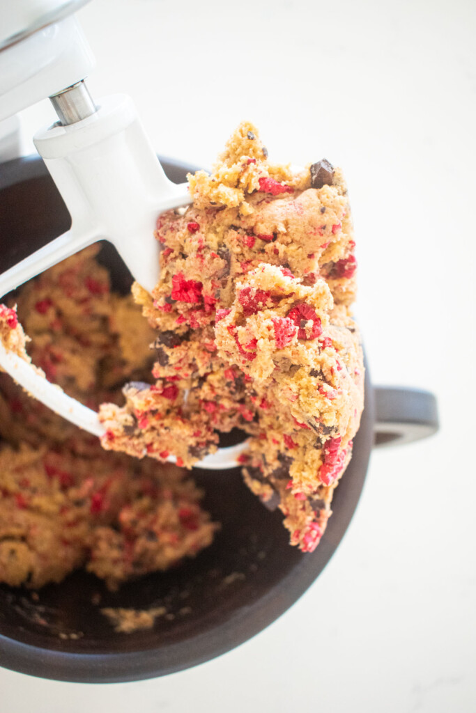 vegan raspberry chocolate chip cookie dough in a wood mixing bowl on a white marble counter.
