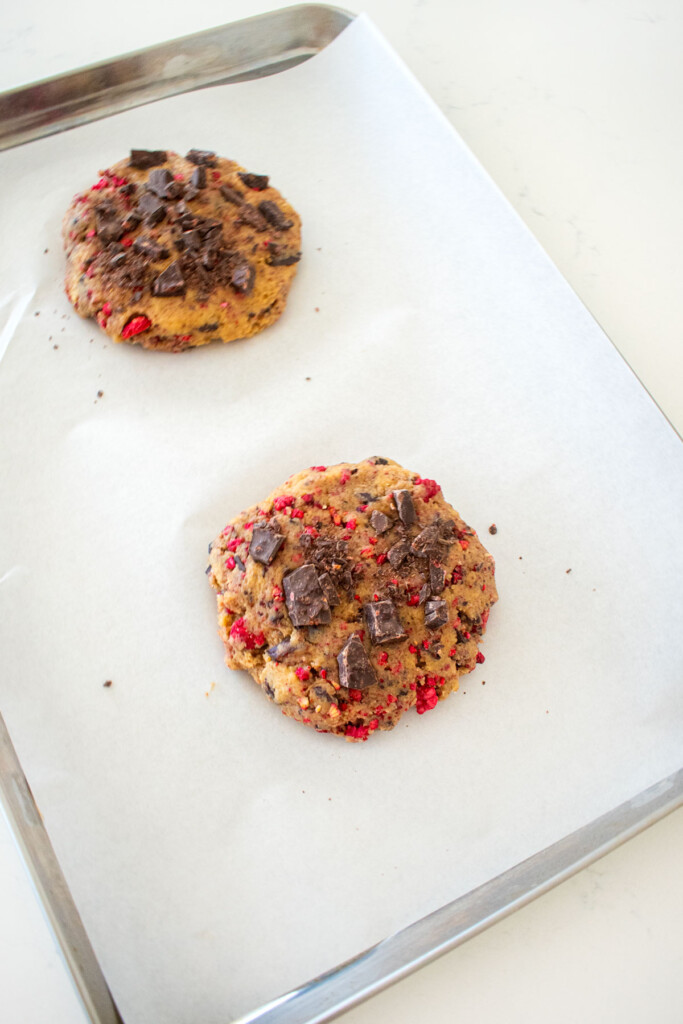 vegan raspberry chocolate chip cookie dough balls on a baking sheet on a white marble counter.