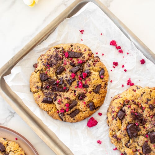 vegan raspberry chocolate chip cookies on a baking sheet on a white marble counter.