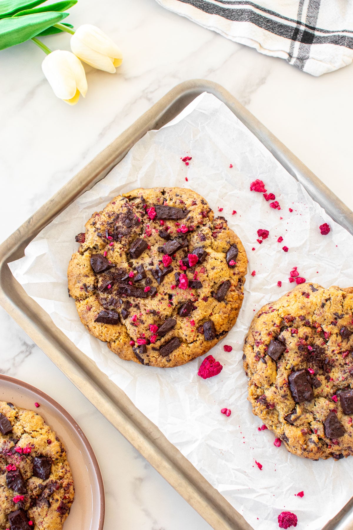 vegan raspberry chocolate chip cookies on a baking sheet on a white marble counter.