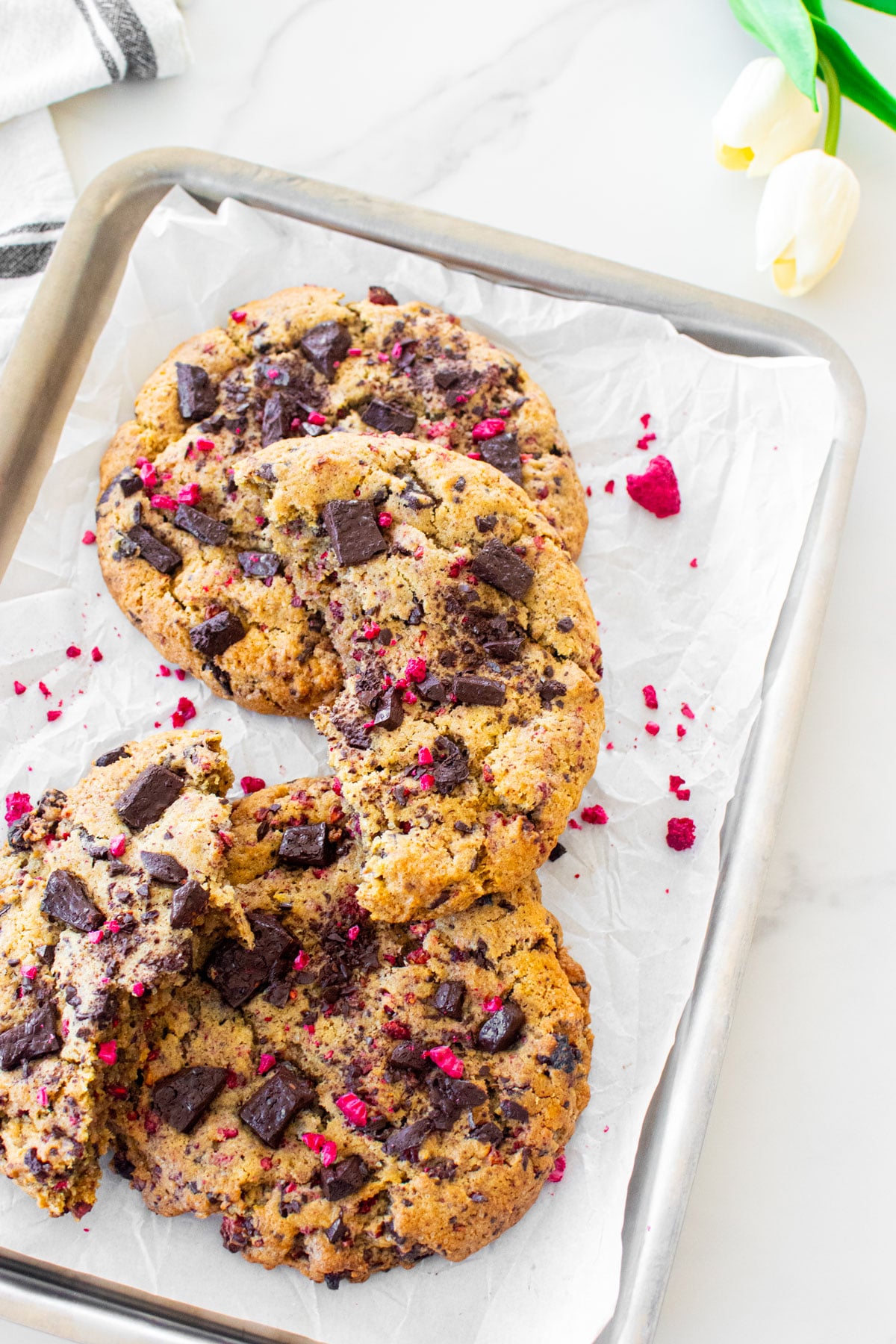 vegan raspberry chocolate chip cookies on a baking sheet on a white marble counter.