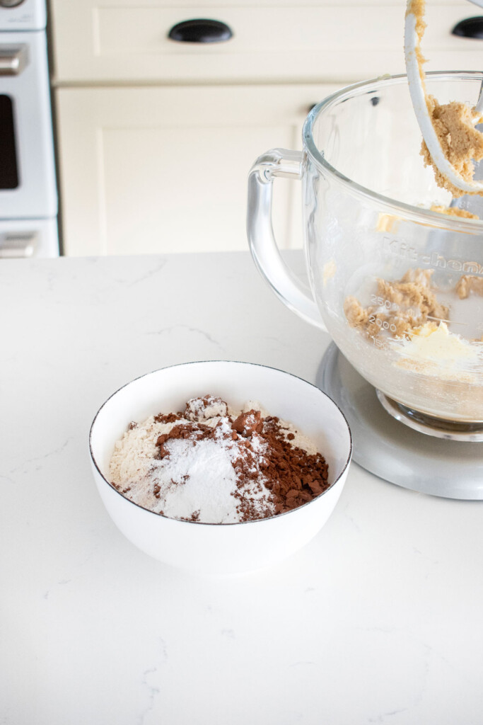 dry ingredients for eggless chocolate chocolate chip cookies in a bowl on a marble counter next to a stand mixer.