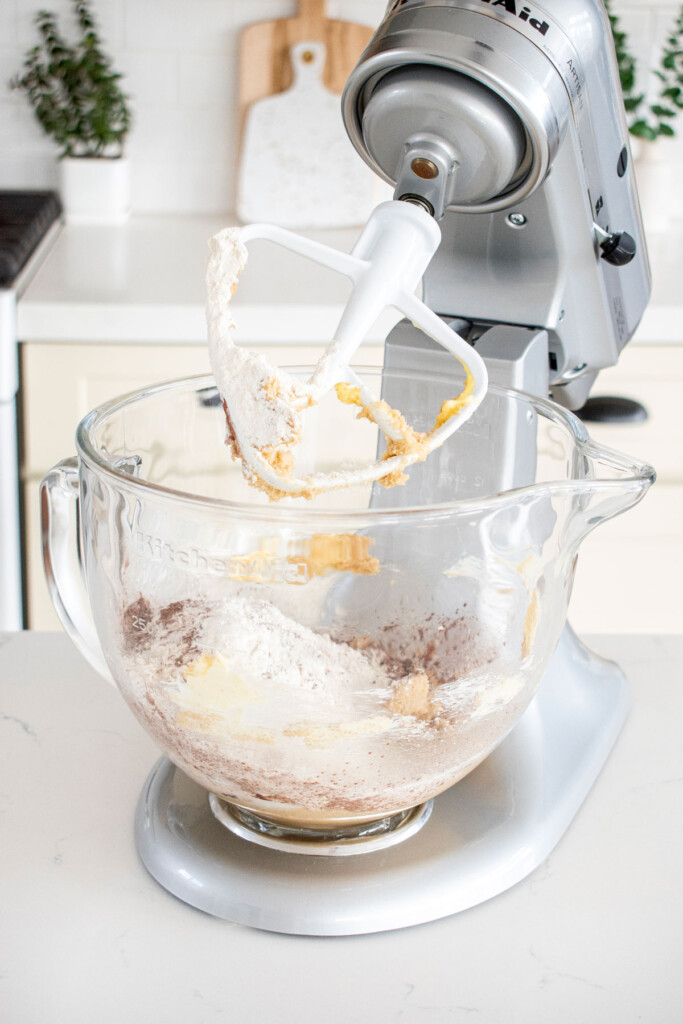 ingredients for eggless chocolate chocolate chip cookies in a stand mixer on a marble countertop.