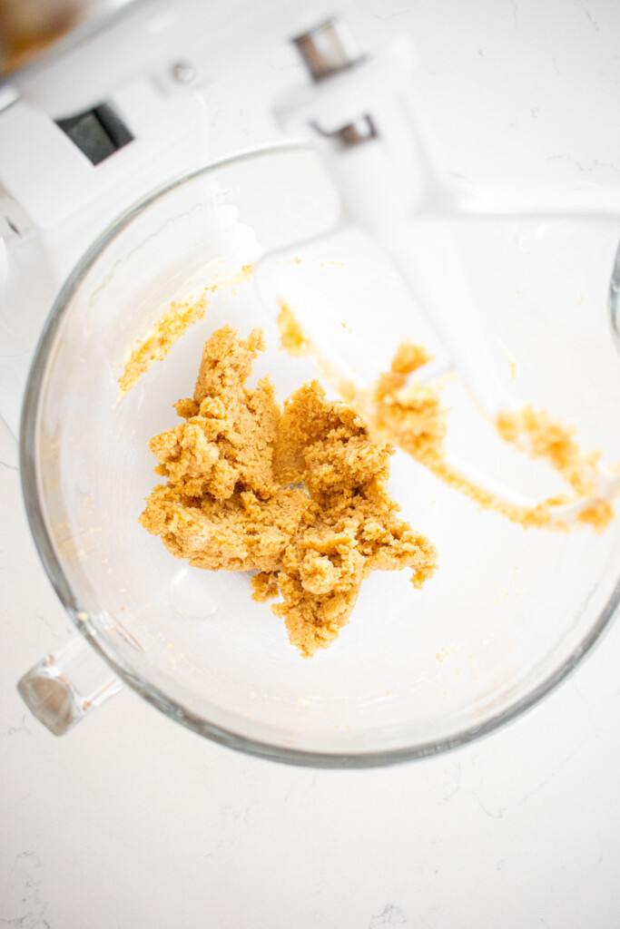 creamed butter and sugar in a glass mixing bowl on a white marble countertop.