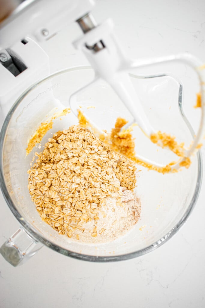 ingredients for eggless oatmeal cookie dough in a glass mixing bowl on a white countertop.