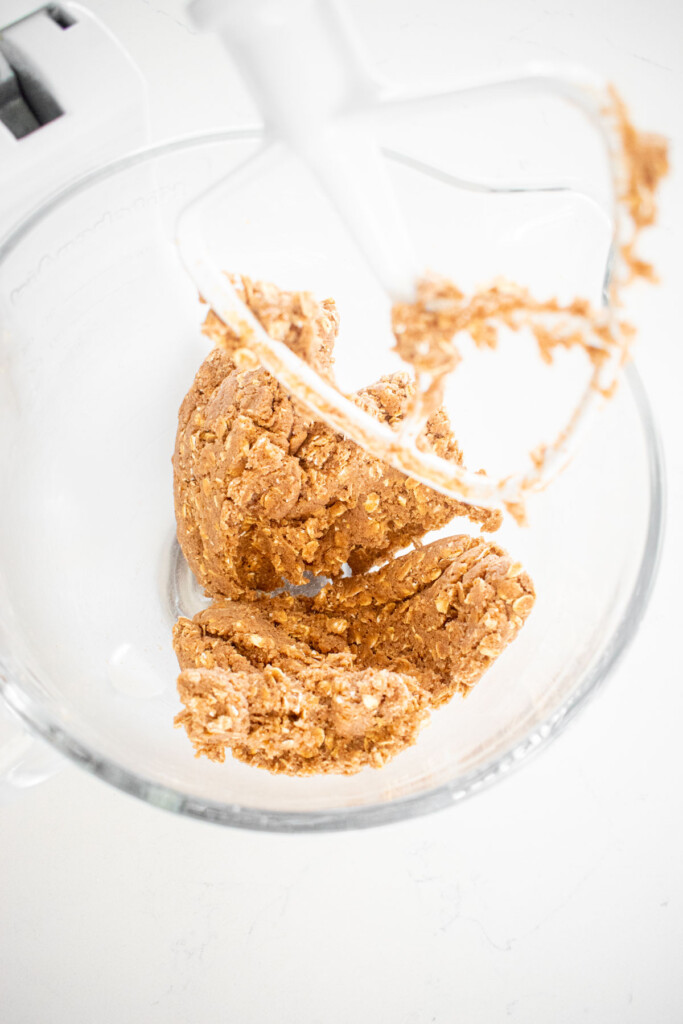 eggless oatmeal cookie dough in a glass mixing bowl on a white marble countertop.