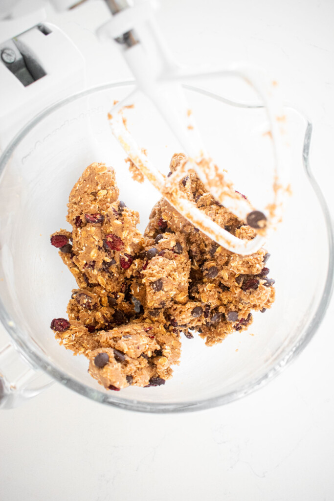 eggless oatmeal cranberry chocolate chip cookie dough in a glass mixing bowl on a white marble countertop.
